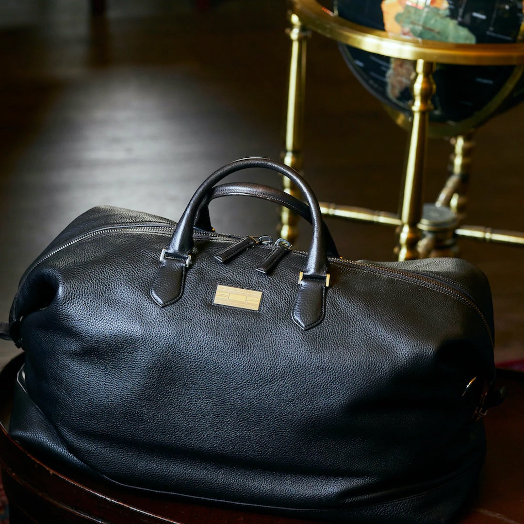 Black leather Aspen travel bag on floor in front of globe - Darby Scott