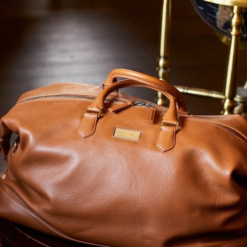 Cognac Leather Aspen Travel Bag on floor in front of globe - Darby Scott