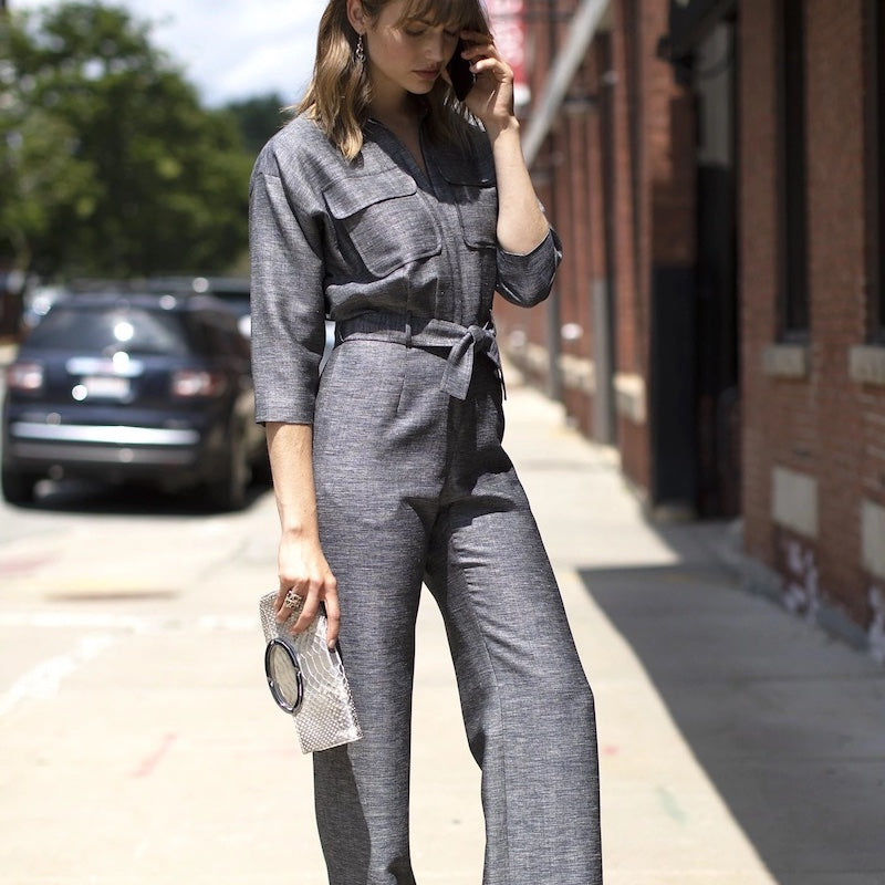 Woman on street wearing navy jumpsuit carrying a fold-over clutch - Darby Scott