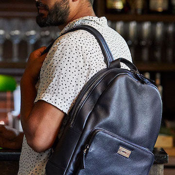 Man in a bar carrying a navy leather Stuart backpack by Darby Scott