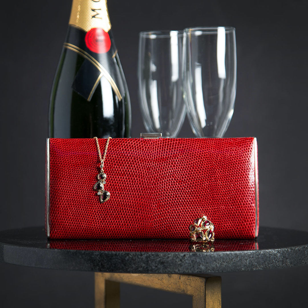 Red lizard wallet, Garnet and diamond ring and pendant on table in front of champagne bottle and glasses