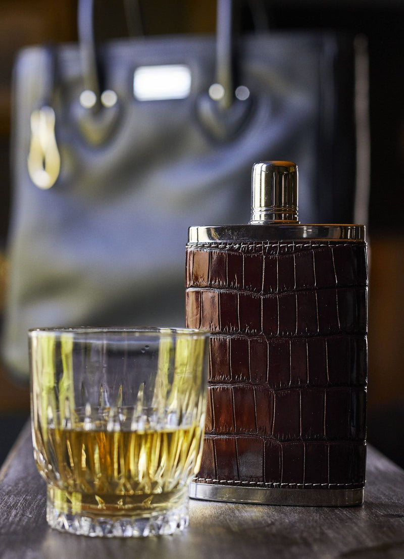 Brown Croc covered hip flask next to a glass - Darby Scott